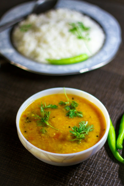 Bowl of arhar with rice and green chilies on a dark surface